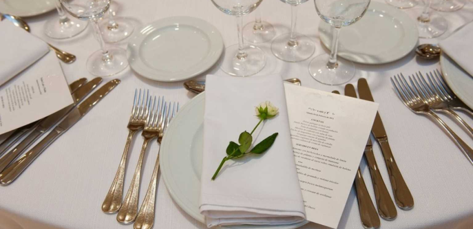 Mesa para banquete preparada con cubiertos, copas, la carta y una flor.