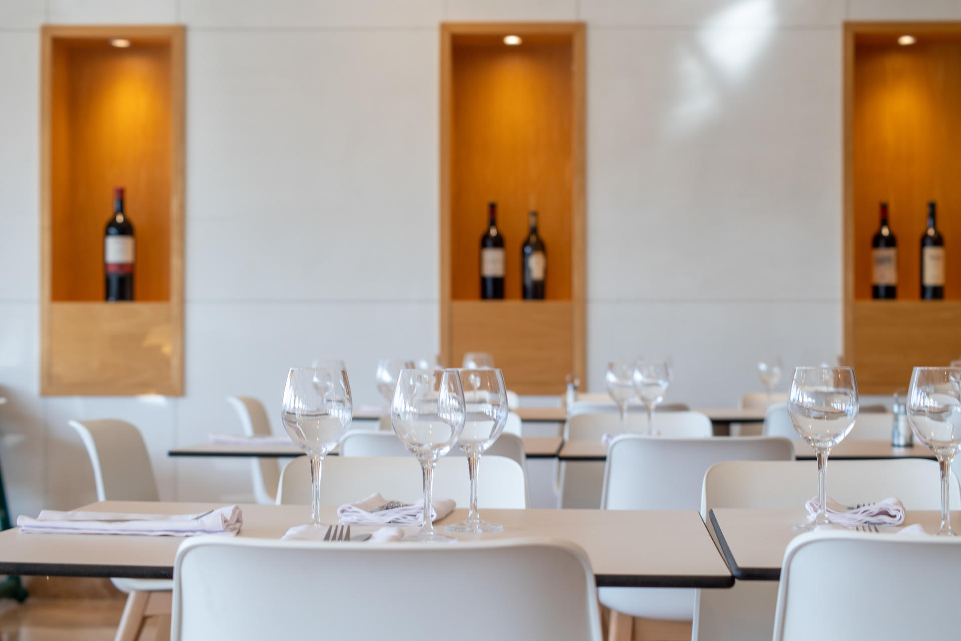 Comedor montado con cubiertos, copas y botellas de vino.